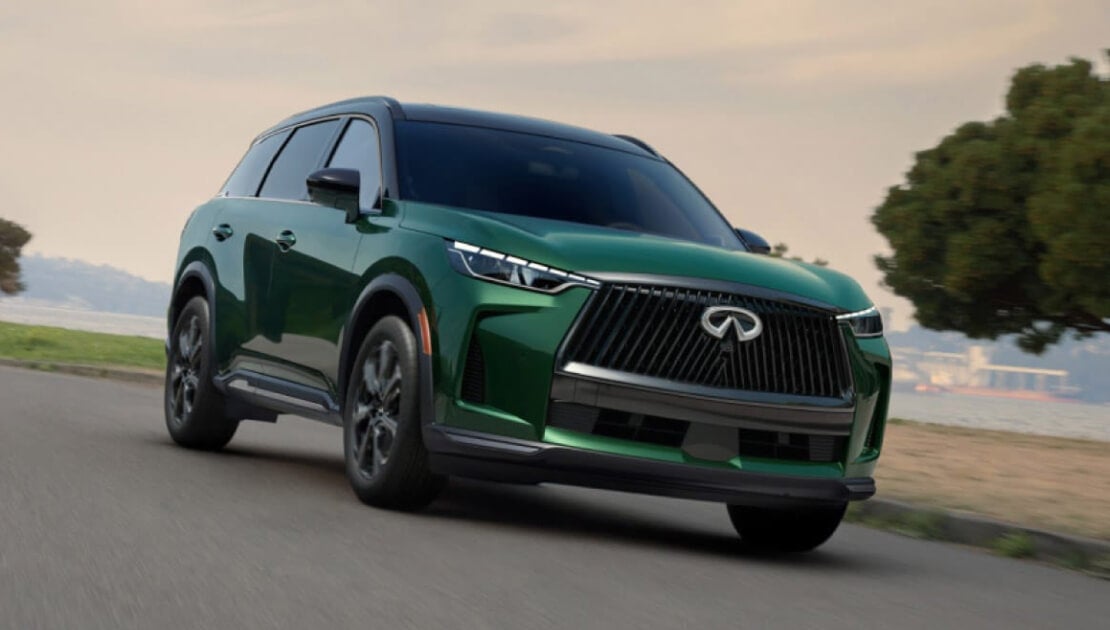 A front view of a green INFINITI QX60 driving down a waterfront road.