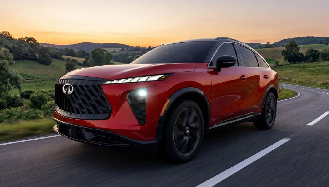A front three quarter view of a red INFINITI QX65 driving down a grassy highway.