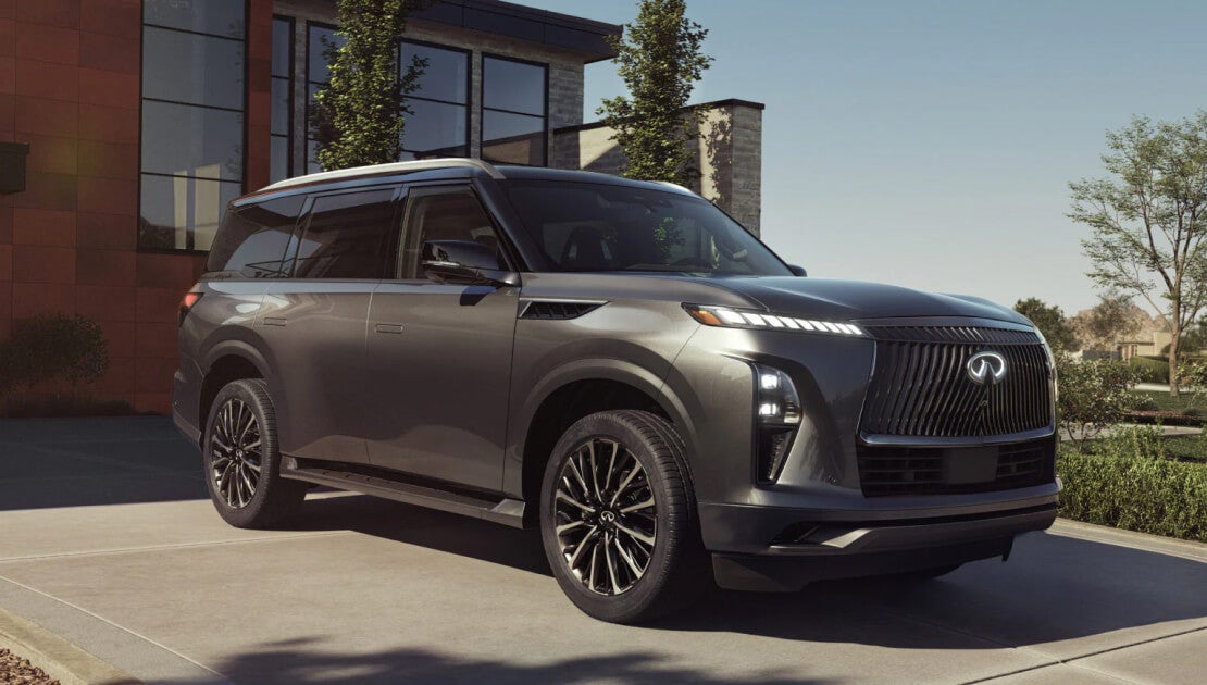 A front three quarter view of a silver INFINITI QX80 parked in an upscale driveway.