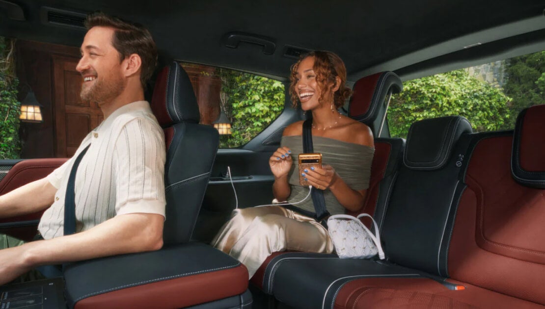 An interior view of the QX80 showing two smiling people comfortably seated in the front and rear passenger seats.