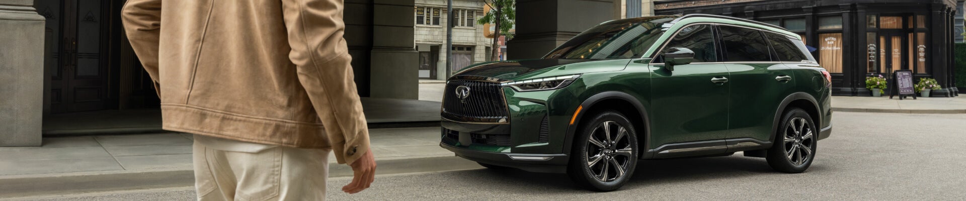 Man in tan jacket standing in front of theatre with a green Infiniti SUV parked on the street
