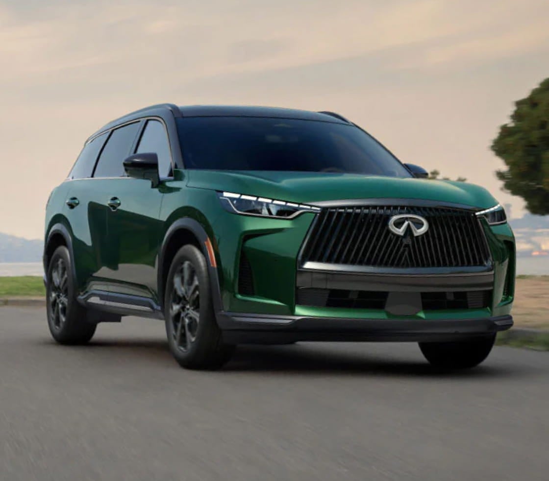 A sleek green Infiniti SUV with a bold front grille and modern headlights drives down a scenic road.